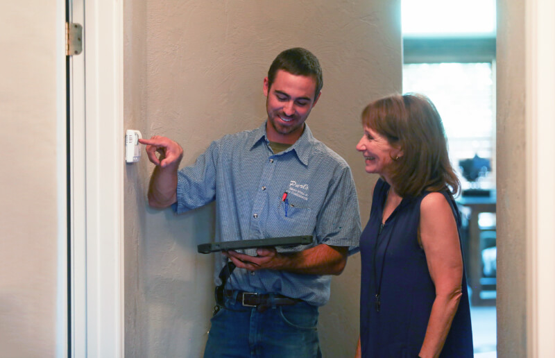 A technician shows a client how to use their thermostat.